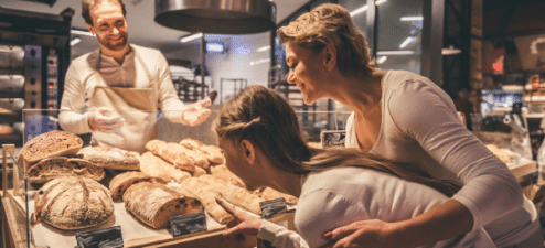 A friendly baker showcasing a variety of fresh bread to two interested customers, illustrating customer engagement strategies to increase foot traffic and customer satisfaction.
